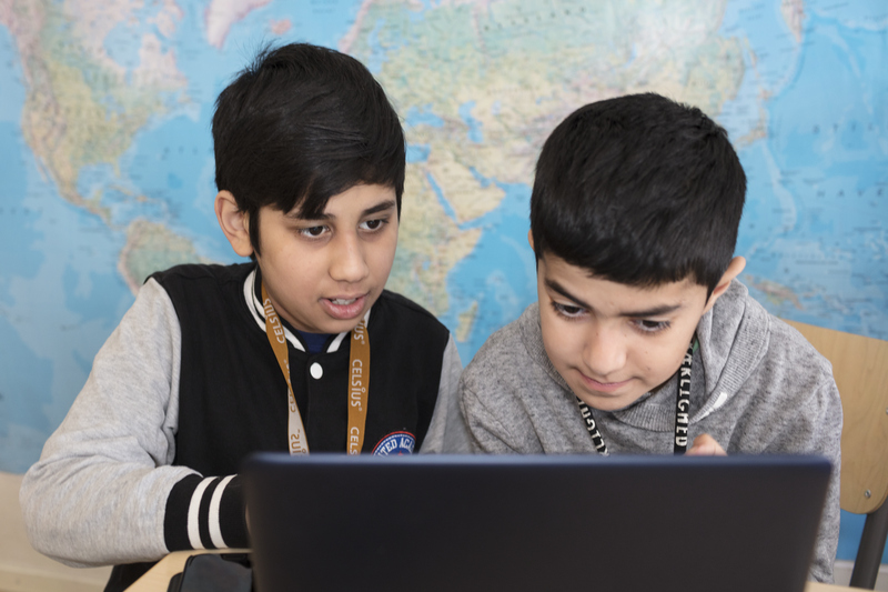 Två elever vid framför en världskarta som tittar på en laptop.
